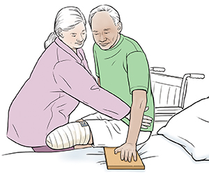 Proveedor de atención médica que ayuda a un hombre con una pierna amputada a usar la tabla de deslizamiento desde la silla de ruedas a la cama.