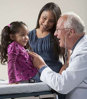 Healthcare provider listening to girl's chest with stethoscope while woman looks on.