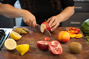 Woman slicing fruit on cutting board.