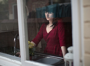 Woman standing in front of a window looking sad.