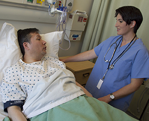 Man in hospital bed talking to healthcare provider.