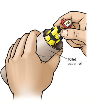 Hand holding toilet paper roll. Another hand inserting small toy into roll.