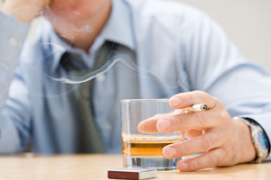 Man smoking cigarette and holding class of whiskey.