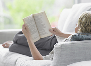 Woman lying on sofa reading a book.