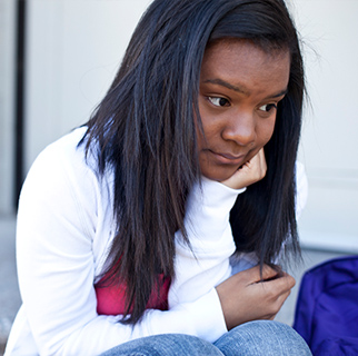 Teenaged girl sitting on steps with a sad look upon her face.