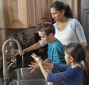 Woman helping boy and girl wash hands in kitchen sink.