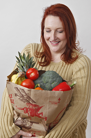Woman holding grocery bag filled with fruits and vegetables.