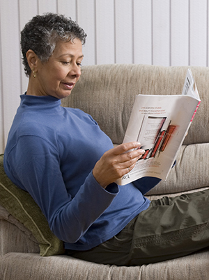 Woman reading magazine on couch with feet elevated.