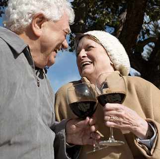 Two senior adults clinking glasses of wine together.