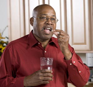 Person taking pill with glass of water.