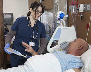 Health care provider caring for man in intensive care unit bed.