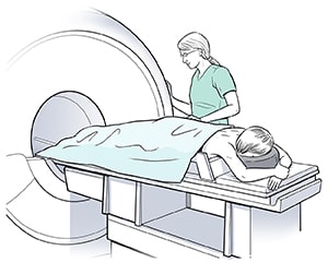Woman lying face down on scanner table, preparing for breast MRI with help of provider.