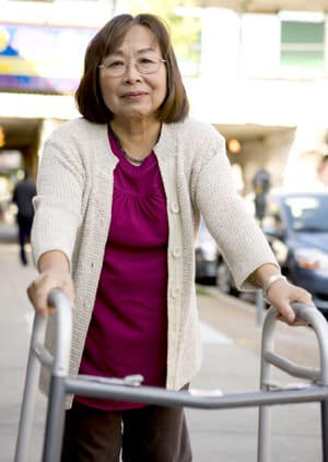 Woman walking with walker on city street.